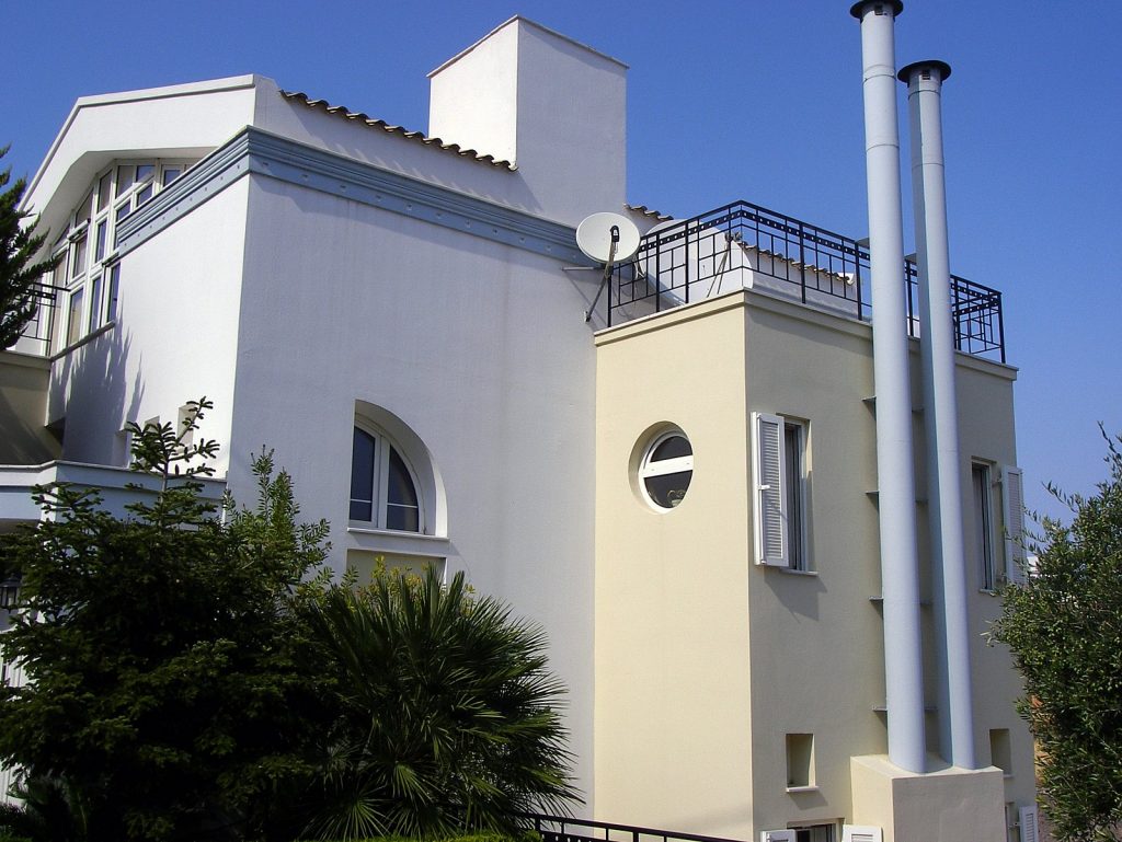 Μοντέρνο πολυώροφο κτίριο με λευκή και μπεζ εξωτερική πρόσοψη. Διαθέτει μεγάλα παράθυρα, κυκλικό παράθυρο και δύο ψηλές κυλινδρικές καμινάδες.